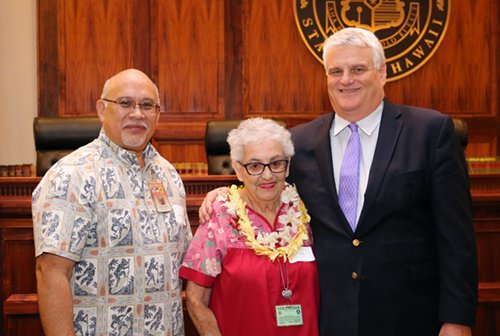Administrative Director of the Courts Rod Maile, Volunteer Millie Botelho, and Chief Justice Mark Recktenwald in front of the bench of the Supreme Court courtroom.