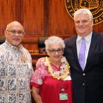 Administrative Director of the Courts Rod Maile, Volunteer Millie Botelho, and Chief Justice Mark Recktenwald in front of the bench of the Supreme Court courtroom.