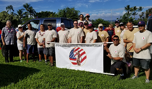 First Circuit Judge Edward Kubo, Jr., and Third Circuit Judge Henry Nakamoto with Veterans Treatment Court associates standing outside on a sunny blue-sky day, on a lawn with a Big Island Veterans Treatment Court banner at the Hilo Veterans Day Parade, 11/09/19.
