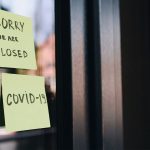 Two post-it notes on a glass door. One says, “Sorry We Are Closed,” the other, “COVID-19.”