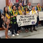 Kauai Drug Court graduates and Deputy Chief Judge Michael K. Soong pose with Friends of Kauai Drug Court and Veterans Court signs in front of the courtroom bench, 05-23-2022.