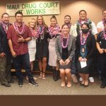 Maui Drug Court team members and seven graduates stand together in the courtroom in front of a sign that says, "Maui Drug Court Works," at the 05/19/2022 graduation ceremony.