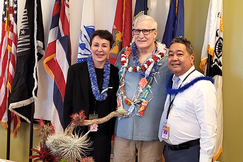 Big Island Veterans Treatment Court Judge Wendy DeWeese, David Riehle, and Chief Judge Robert Kim stand in front of the U.S., State of Hawaii, and military branch flags at the Kona courthouse, July 11, 2022.