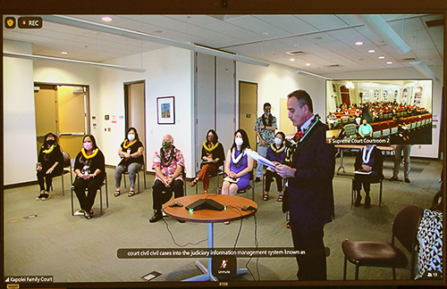 Members of the First Circuit (Oahu) Family Court Civil JIMS Team sit in chairs in the Ronald T.Y. Moon Judiciary Complex Multi-Purpose Room as First Circuit Deputy Chief Judge and Senior Family Court Judge Matthew Viola stands at the front reading the 2022 Group Meritorious Service Award proclamation.