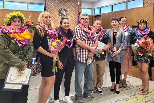 Kona Drug Court Presiding Judge Wendy DeWeese and seven Big Island Drug Court graduates stand together in front of the courtroom bench, 10/24/2022.