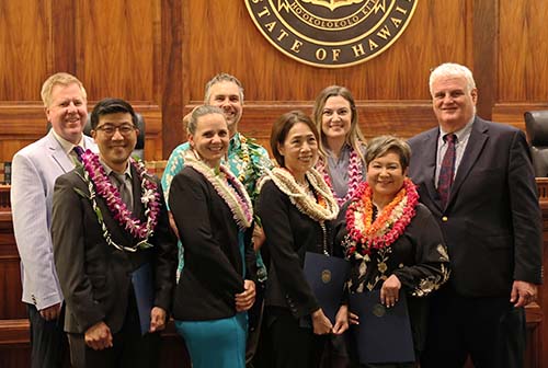 Hawaiʻi Supreme Court Associate Justice Todd Eddins, attorneys Daniel Kawamoto, Maile Osika, Zachary McNish, Lily Ling, Madisson Heinze, Marie Laderta, and Chief Justice Mark Recktenwald standing together in front of the Hawaiʻi Supreme Court courtroom bench at the Hawaiʻi Access to Justice Commission's 2023 Pro Bono Celebration, 10/26/2023.