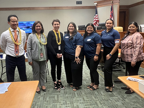Third Circuit District Family Court Judges Jeffrey Ng and Darien Ching Nagata, Chief Judge Wendy DeWeese, HI H.O.P.E.S. President Melissa Mayo, Vice President Tianna Ceils-Webster, Secretary Precious Ahulau-Kaleo, and Advisor Raquel Gali standing together in front of the Courtroom 3C bench, at the Hale Kaulike courthouse on East Hawaiʻi Island Teen Day, July 31, 2024.