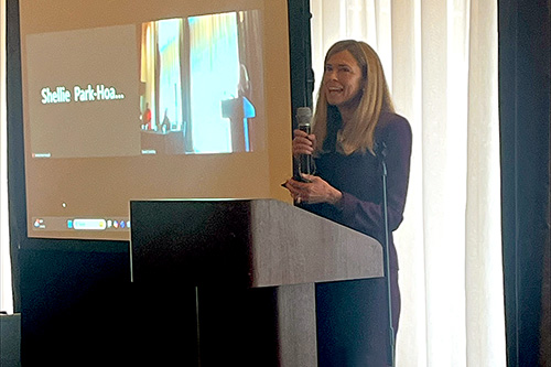 Judge Erika Ireland speaking from the podium at the 2025 Fair Housing for Our Future Laws & Litigation Conference in San Diego, California, with Shellie Park-Hoapili's name on Zoom projected on the screen positioned to the left of Judge Ireland, 02-13-2025.