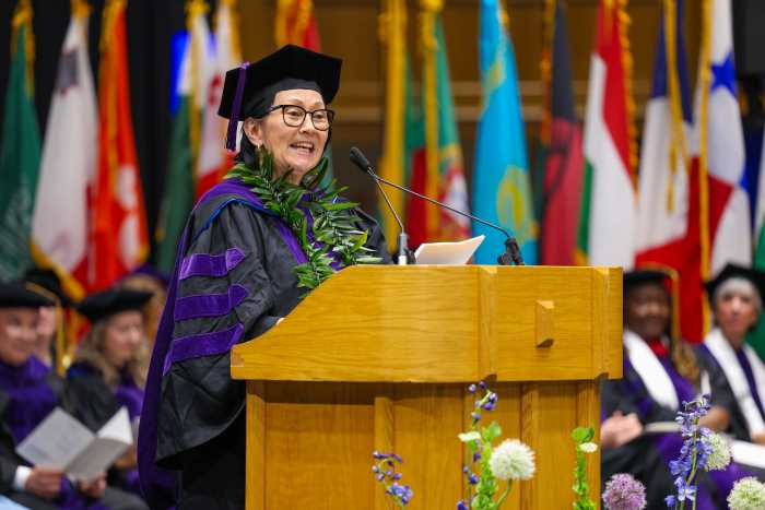 Hawaiʻi Supreme Court Associate Justice Sabrina McKenna wears a purple and black graduation cap and gown while standing behind a podium on a stage at Cameron Indoor Stadium on the Duke University campus during her speech to fellow graduates and others gathered for Duke Law’s convocation ceremony on May 10, 2025.