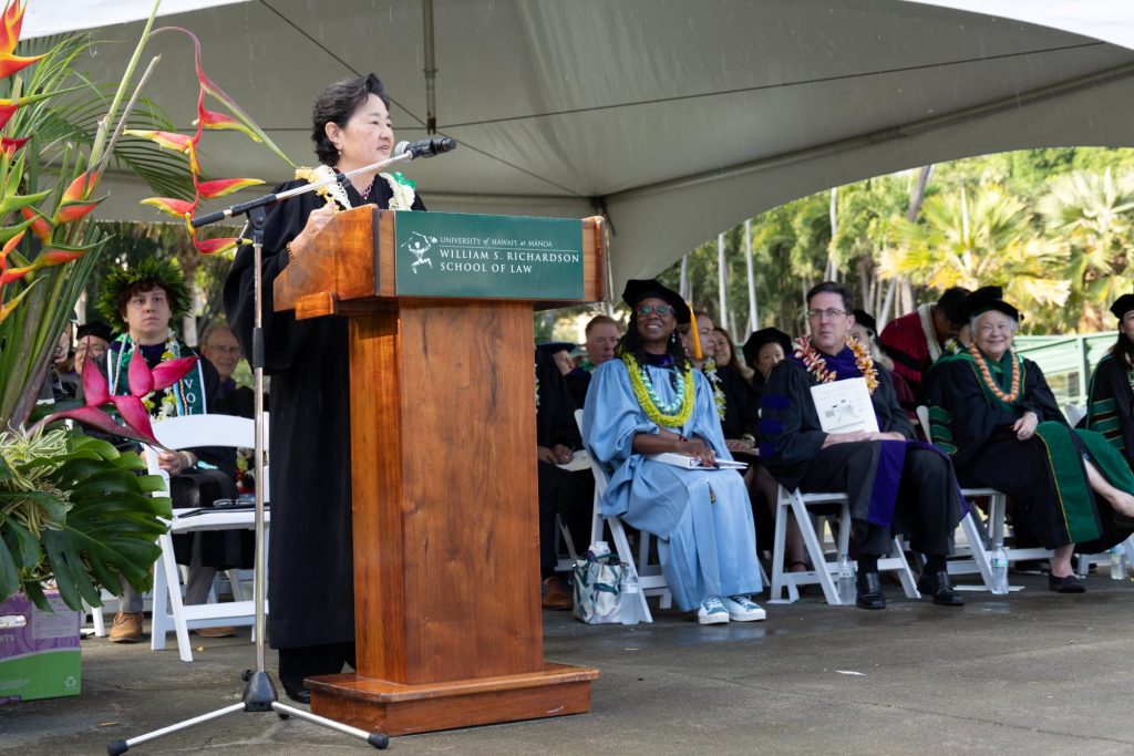 Hawaiʻi Supreme Court Associate Justice Lisa M. Ginoza stands behind a podium on stage at Andrew Amphitheater while delivering the keynote address to graduates of the University of Hawaiʻi William S. Richardson School of Law on May 18, 2025.