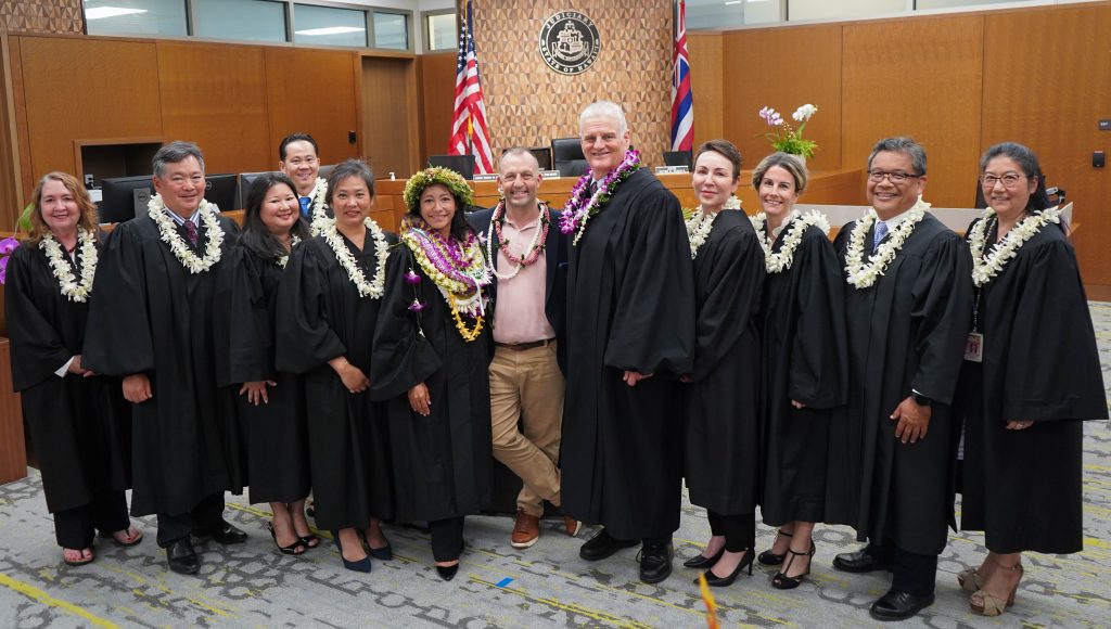 New Circuit Judge Kauanoe A.D. Jackson poses for a photograph with Hawaii Governor Josh Green, Hawaii Supreme Court Chief Justice Mark Recktenwald and nine other judges from Hawaii Island after Jackson’s swearing-in ceremony at the Keahuolū Courthouse in Kailua-Kona on June 2, 2025. The judges are all wearing black robes.  Governor Green is wearing a sport coat over a pink shirt.  Everyone is wearing at least one lei.