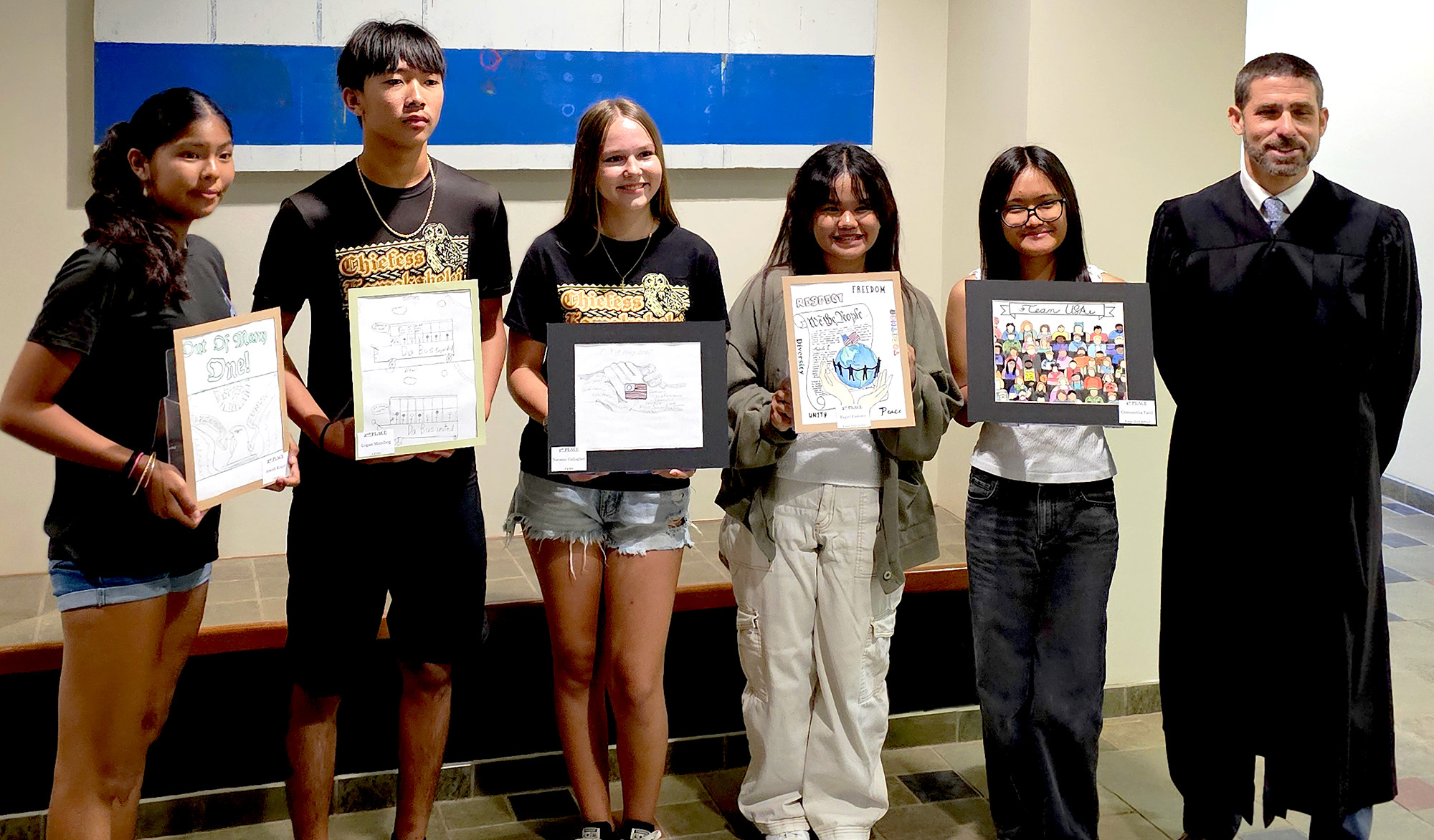 Hawaiʻi’s Fifth Judicial Circuit 2025 Law Day Art Contest winners holding their artwork. From left: Chiefess Kamakahelei Middle School eighth grade students Araceli Ringor, Logan Manibog, and Naomi Gallagher, with Kauaʻi High School Grade 9 students Pagiel Ramire and Czamantha Tabil, and Fifth Circuit District Court Judge Gregory H. Meyers, 05/13/2025.