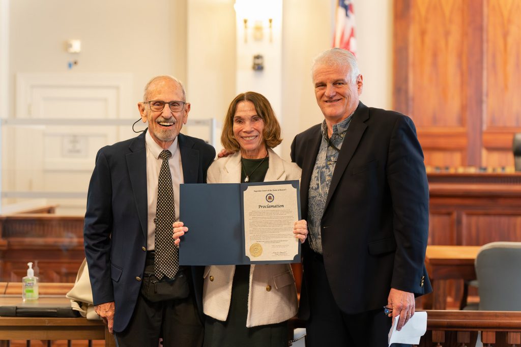 Family law attorney William C. Darrah and The Mediation Center of the Pacific’s Executive Director Tracey S. Wiltgen (holding up a copy of the chief justice’s proclamation), and Hawaiʻi Supreme Court Chief Justice Mark E. Recktenwald, in the Hawaiʻi Supreme Court courtroom for a presentation commemorating the 300th Seminar of Divorce Law in Hawaiʻi, 07-16-2025.