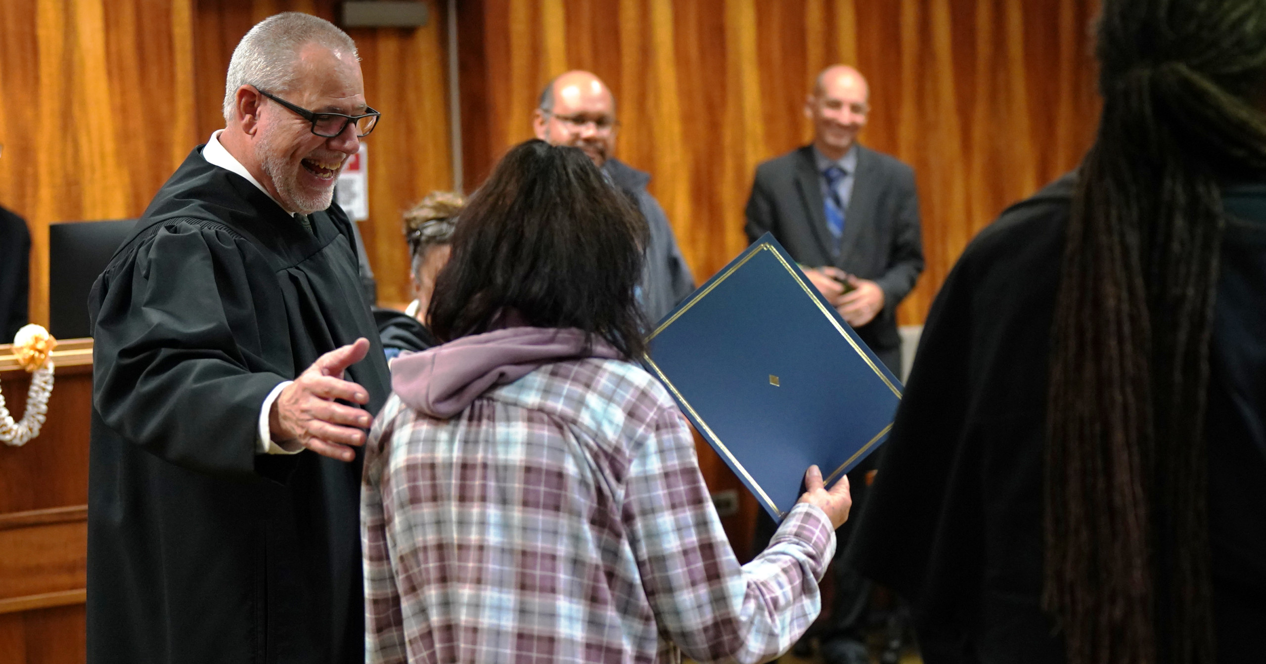 Circuit Court Judge Ronald Johnson presents a certificate of completion to an Oʻahu Post-Booking Jail Diversion Program graduate.