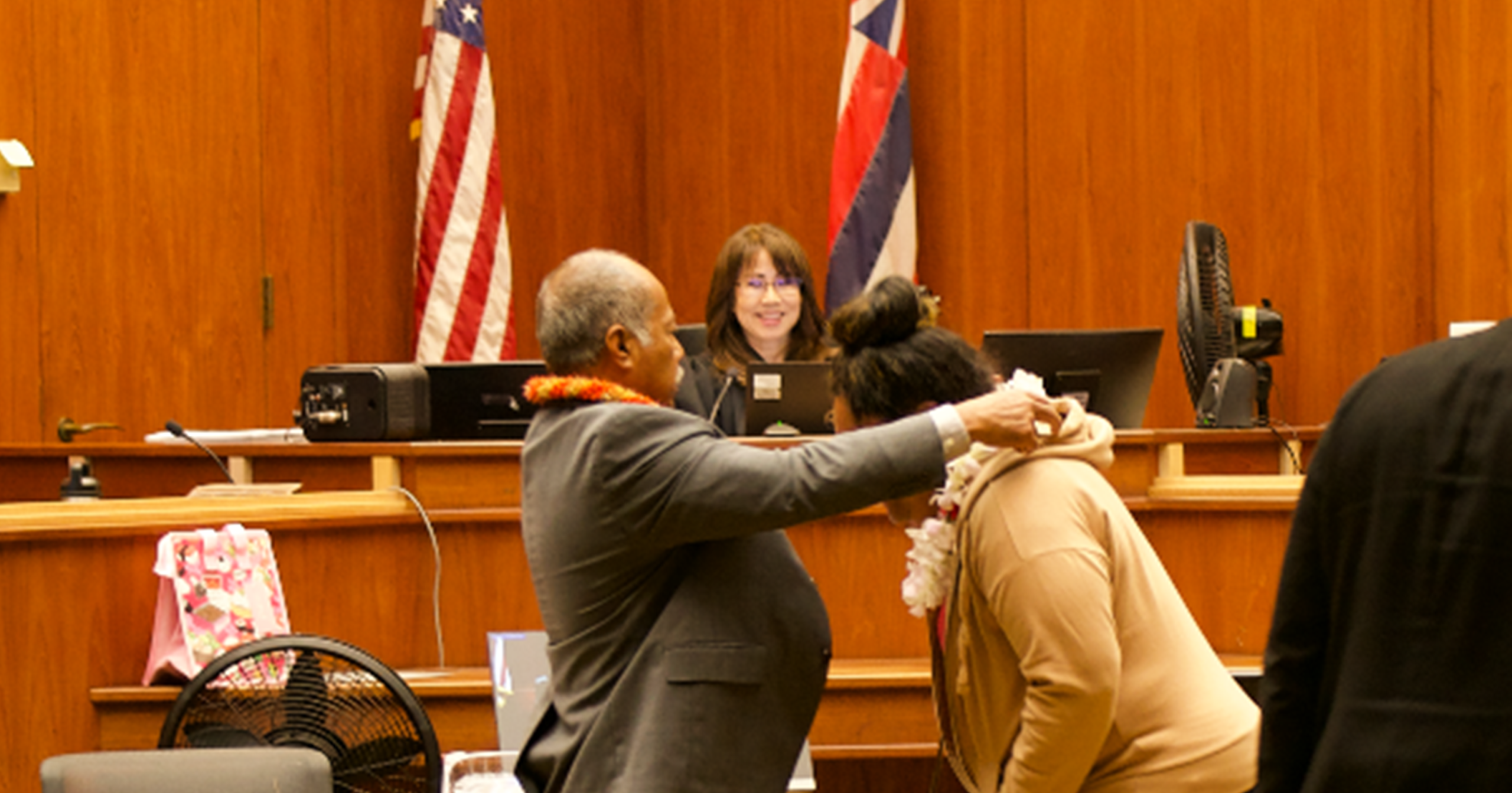 District Court Judge Tracy Fukui looks on as Deputy Public Defender Jerry Villanueva presents lei to an Oʻahu Post-Booking Jail Diversion Program graduate.